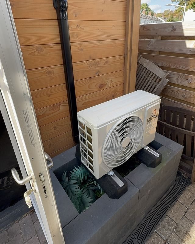 Buitenunit van de airco op een stenen verhoging naast de schuur