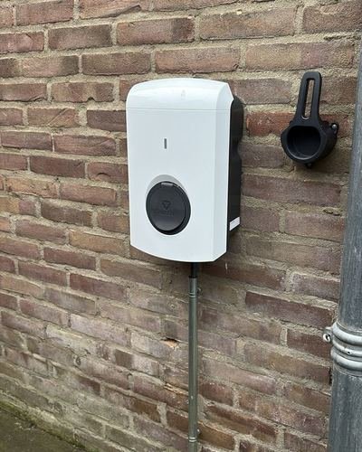 Witte laadpaal aan een bakstenen gevel in Valthe